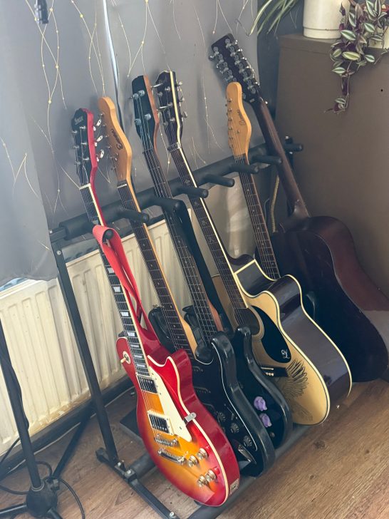 A collection of six guitars, including electric and acoustic styles, on a stand.